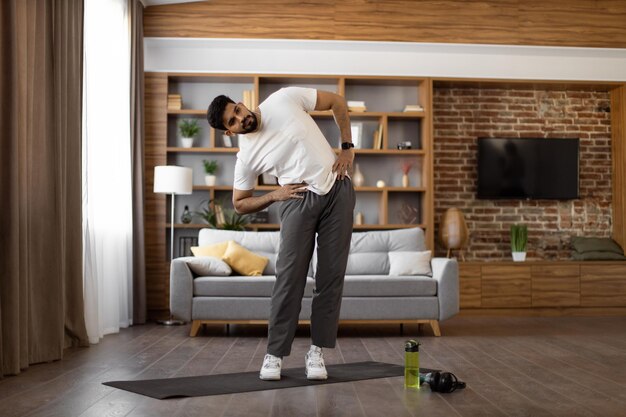 Foto hombre indio haciendo inclinaciones laterales con las manos en las caderas en casa