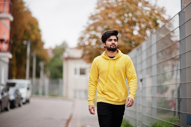 Hombre indio joven hipster urbano en una sudadera amarilla de moda Cool chico del sur de Asia usa sudadera con capucha caminando en la calle de otoño