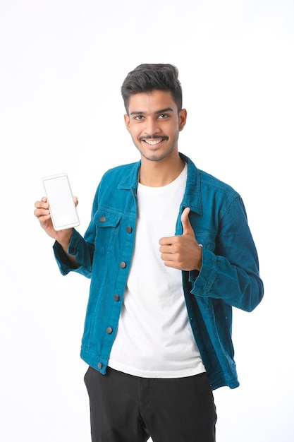 Hombre indio joven que muestra la pantalla del teléfono inteligente sobre fondo blanco.