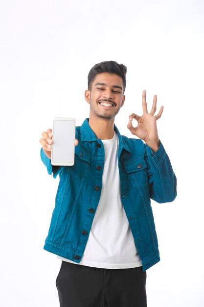 Hombre indio joven que muestra la pantalla del teléfono inteligente sobre fondo blanco.