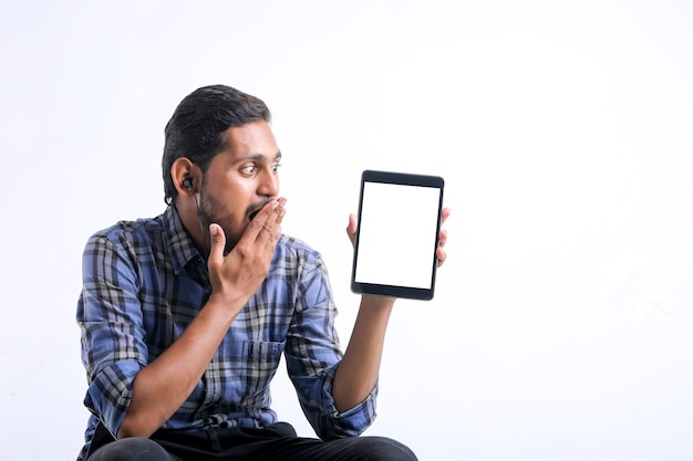 Hombre indio joven que muestra la tableta sobre el fondo blanco.