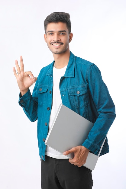 Hombre indio joven que sostiene la computadora portátil en la mano sobre fondo blanco.