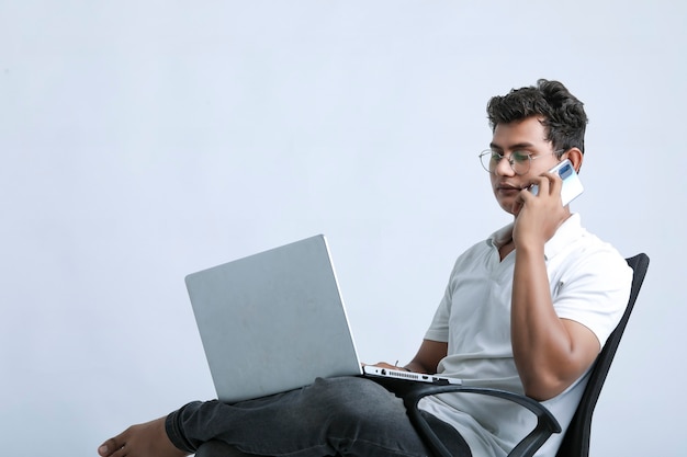 Hombre indio joven que trabaja en la computadora portátil y que usa el teléfono inteligente.