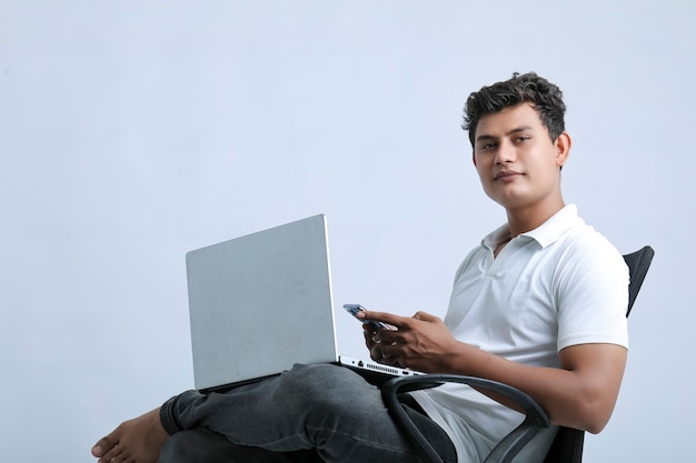 Hombre indio joven que trabaja en la computadora portátil y que usa el teléfono inteligente.