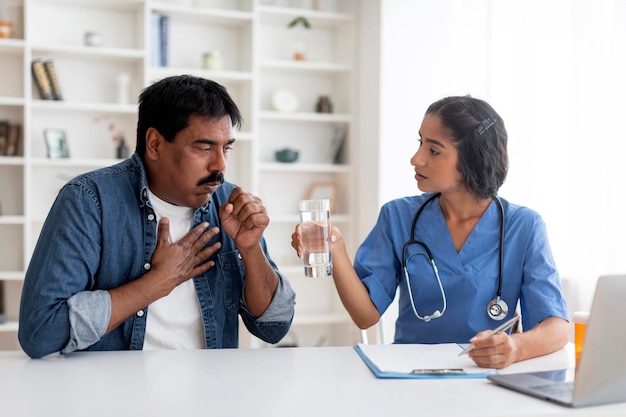 Hombre indio maduro enfermo tosiendo durante una reunión con una doctora en la clínica