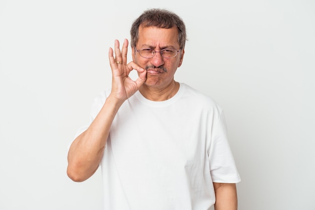 Hombre indio de mediana edad aislado sobre fondo blanco con los dedos en los labios guardando un secreto.