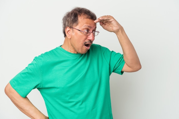 Hombre indio de mediana edad aislado sobre fondo blanco mirando lejos manteniendo la mano en la frente.