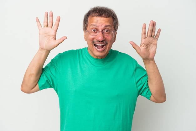 Hombre indio de mediana edad aislado sobre fondo blanco recibiendo una agradable sorpresa, emocionado y levantando las manos.