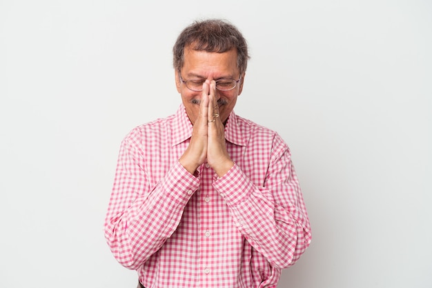 Hombre indio de mediana edad aislado sobre fondo blanco tomados de la mano en oración cerca de la boca, se siente confiado.