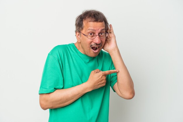 Hombre indio de mediana edad aislado sobre fondo blanco tratando de escuchar un chisme.