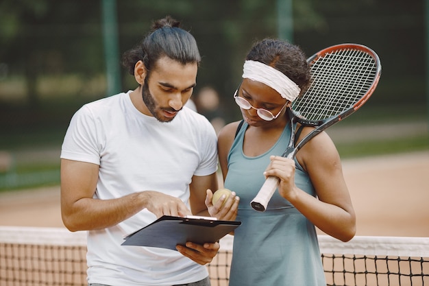 Hombre indio y mujer negra americana de pie en una cancha de tenis