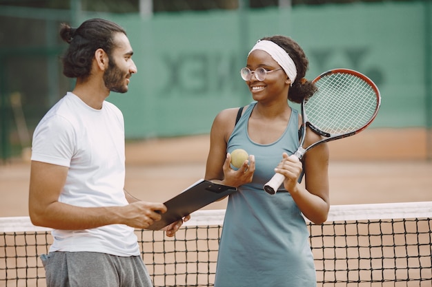 Hombre indio y mujer negra americana de pie en una cancha de tenis