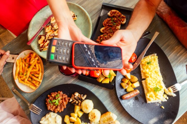 Hombre indio que paga en un restaurante con una aplicación de tarjeta de crédito en un lector de teléfonos inteligentes