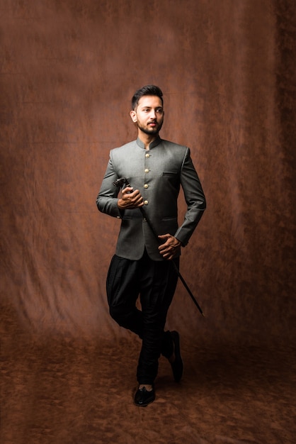 Hombre indio en ropa tradicional o kurta, telas de pijama. Modelo masculino en sherwani, posando o de pie contra el fondo marrón grunge, enfoque selectivo