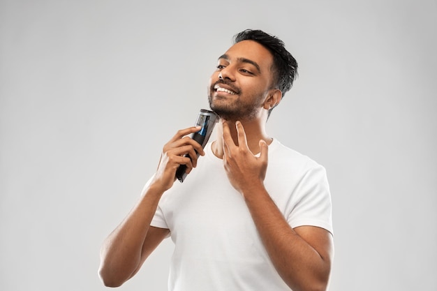 hombre indio sonriente afeitando la barba con un cortador