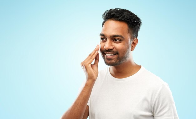Hombre indio sonriente limpiando la cara con una almohadilla de algodón