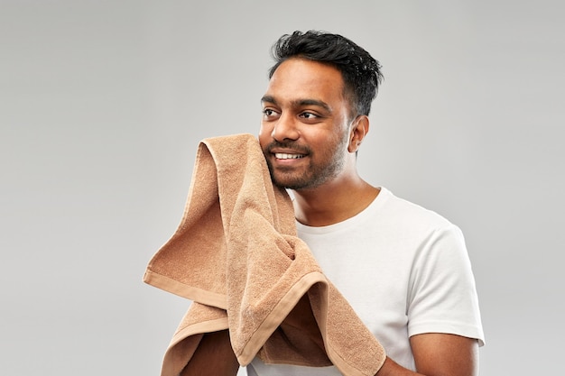 hombre indio sonriente con toalla sobre fondo gris