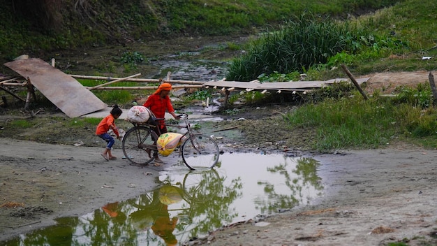 un hombre indio trae su bicicleta con su hijo a través del agua sucia Siwan Bihar India 28 febrero 2024