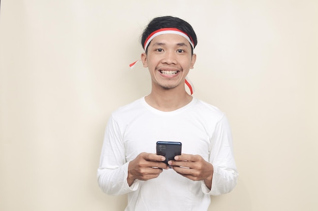 Hombre indonesio sonriendo mientras sostiene un teléfono móvil durante la celebración del día de la independencia