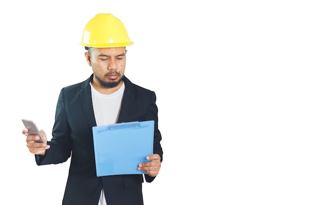 Hombre de ingeniería asiática lleva casco con smartphone y papeleo sobre fondo blanco. capataz de control de la construcción. trazado de recorte.