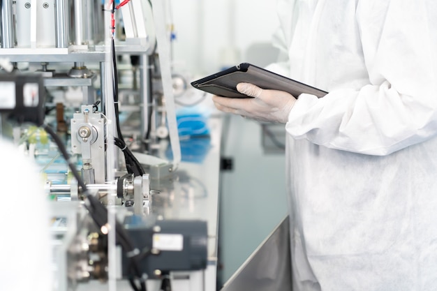 Hombre de ingeniería profesional en paños estériles y máquina de trabajo y control de mascarilla en la fábrica de mascarillas quirúrgicas. concepto de fábrica y personas de la industria. adentro