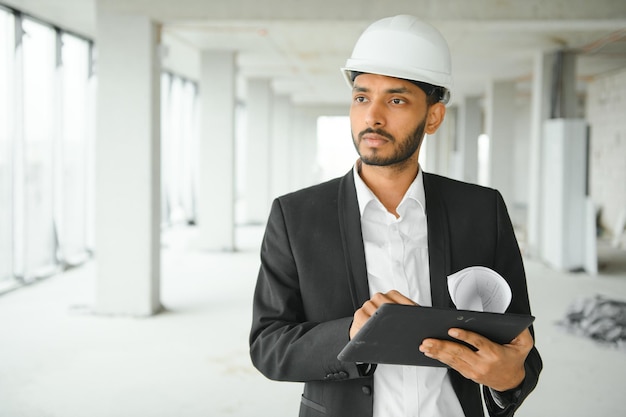 Foto hombre ingeniero asiático confiado que usa tableta para verificar y mantener para inspeccionar en la construcción de viviendas modernas arquitecto que trabaja con casco de seguridad blanco en el sitio de construcción