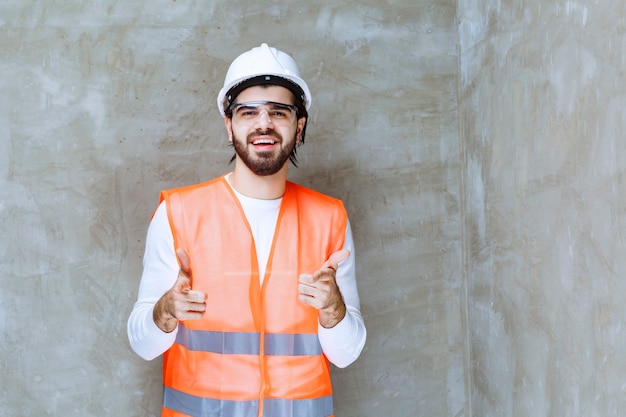 Hombre ingeniero con casco blanco y anteojos protectores apuntando a su colega o algo a un lado.