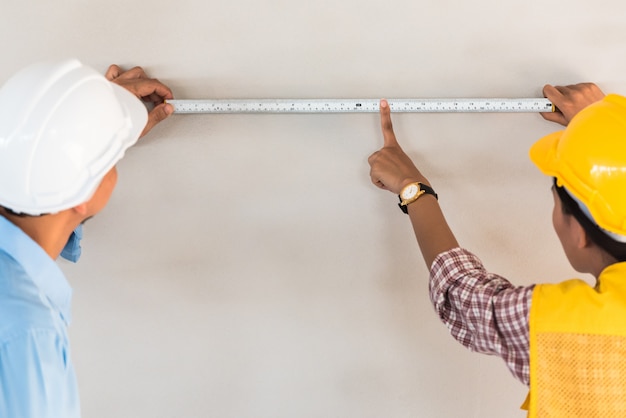 Hombre ingeniero con cinta métrica en la pared en el sitio de construcción de edificios.