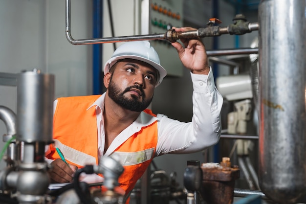 Hombre ingeniero con gafas mientras revisa y repara la máquina de presión de la caldera de tubería en la fábrica de bebidas