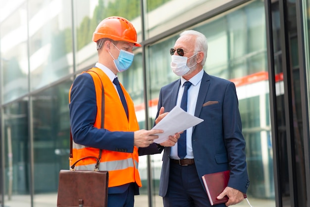 Hombre ingeniero con máscara discutiendo algo con un hombre de negocios senior con máscara