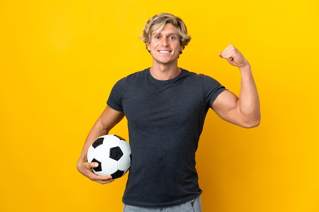 Hombre inglés sobre pared amarilla aislada con balón de fútbol celebrando una victoria