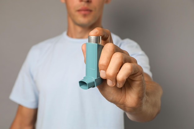Hombre con inhalador de asma en primer plano de fondo gris