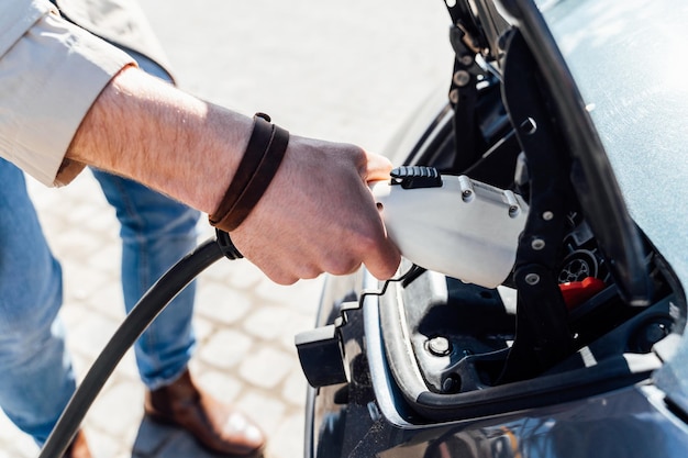 El hombre inserta el enchufe del cargador en el enchufe del primer plano del coche eléctrico