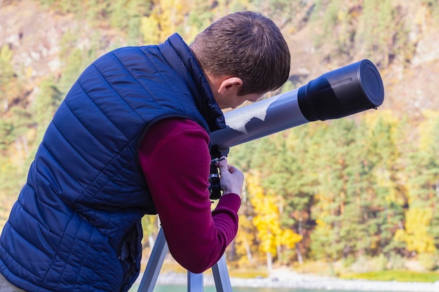 El hombre instala un telescopio en un trípode para inspeccionar el paisaje otoñal de las montañas y las estrellas en el cielo nocturno