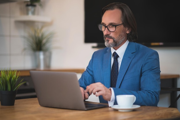 Hombre inteligente apuesto con anteojos trabajando en una laptop