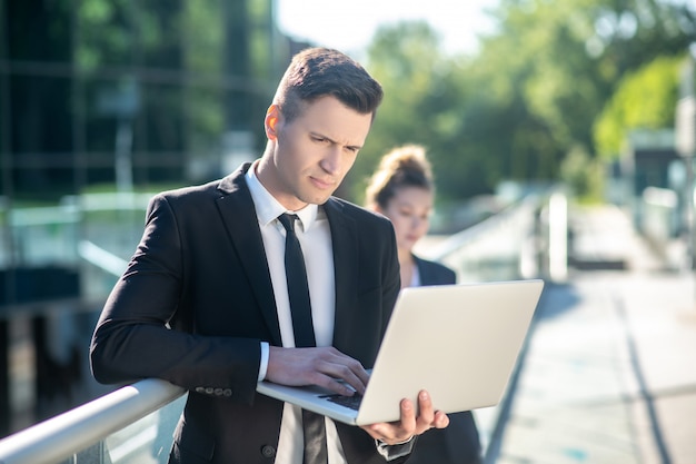 Hombre inteligente atento mirando una computadora portátil en la calle