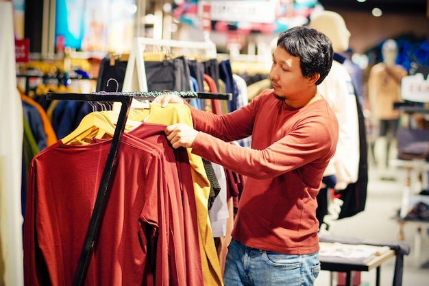 Hombre inteligente con barba elegir ropa en tienda de ropa en el centro comercial