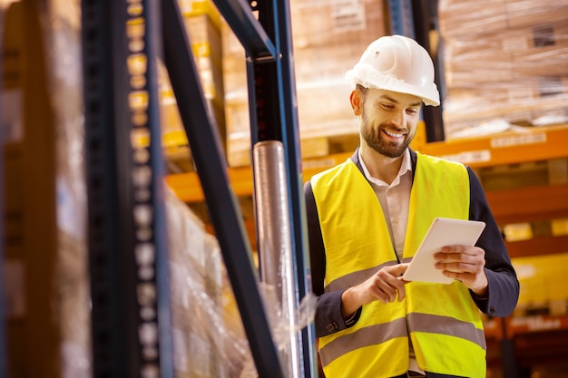 Hombre inteligente positivo mirando su tableta mientras hace el control de inventario