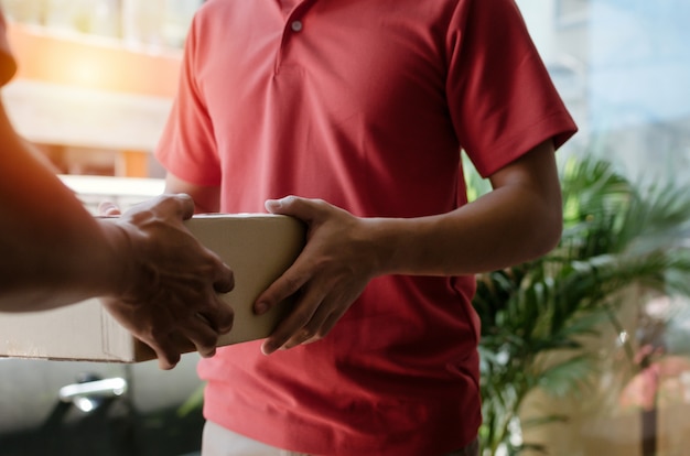 Hombre inteligente del servicio de entrega a domicilio en uniforme rojo entregando cajas de paquetes al destinatario y al cliente joven