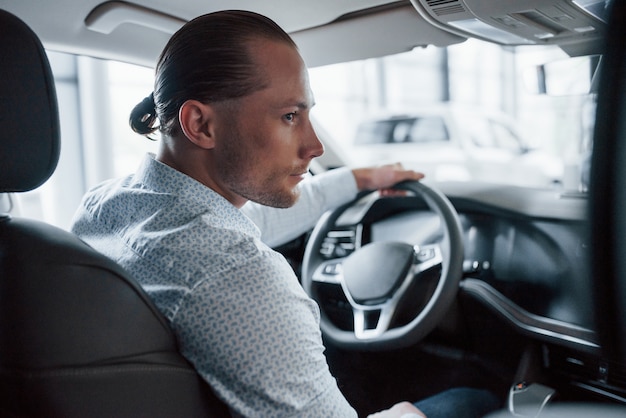 Hombre intentando coche nuevo en el salón durante el día. Comprar vehículo nuevo