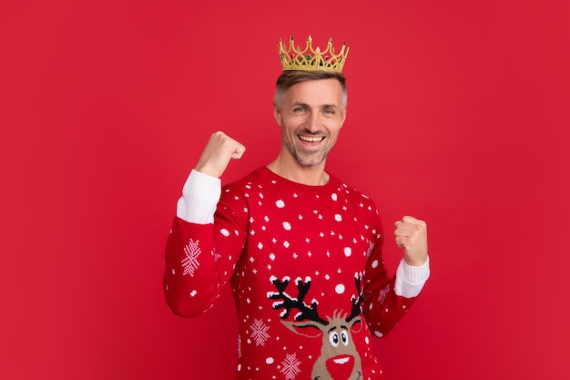 Hombre de invierno en corona Retrato de hombre de mediana edad en suéter aislado sobre fondo rojo Concepto de vacaciones felicidad emociones y celebración de Navidad