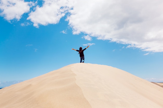 Hombre irreconocible con los brazos abiertos en la cima de una duna del desierto. Hombre disfrutando de la libertad.