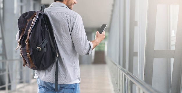 Hombre irreconocible caminando en la terminal del aeropuerto y usando un teléfono inteligente navegando por Internet