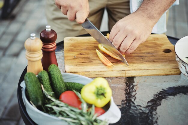 Hombre irreconocible cortando pimienta dulce para ensalada