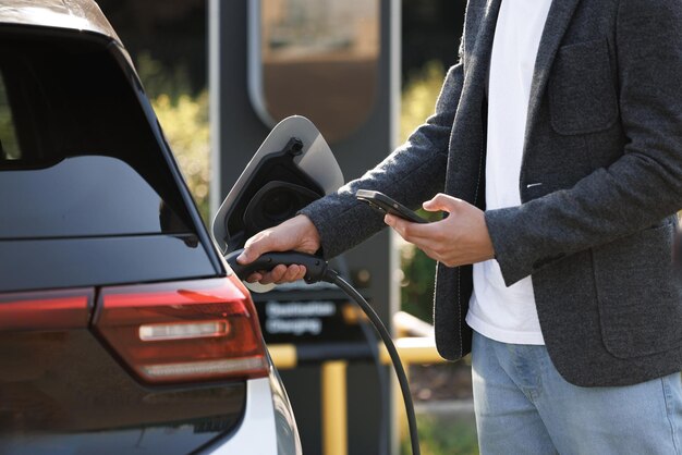 Foto hombre irreconocible enchufando coche eléctrico de la estación de carga hombre enchufando el cable de alimentación a