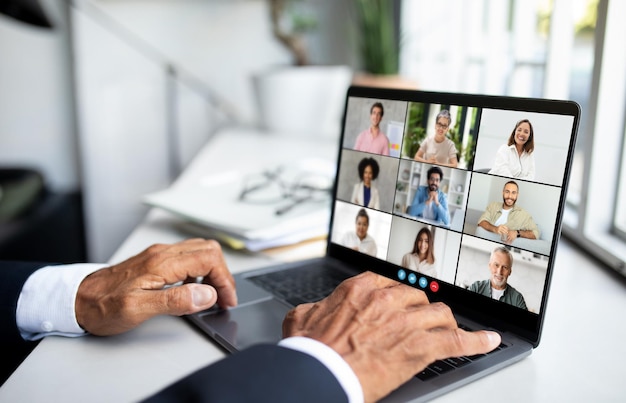 Un hombre irreconocible está sentado frente a una computadora portátil participando en una llamada de video con un grupo de personas