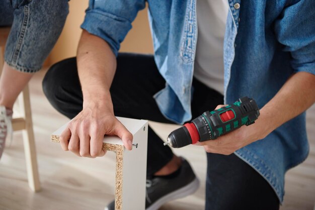 Hombre irreconocible instalando muebles blancos.