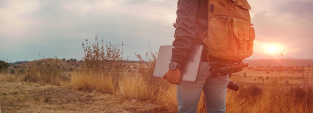 Hombre irreconocible con una laptop caminando al atardecer