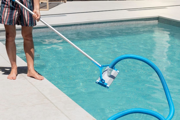 Hombre irreconocible limpiando la piscina con un limpiador automático de piscinas en el patio trasero de su casa