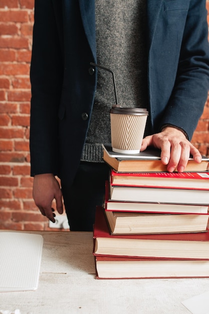 Foto hombre irreconocible parado en libros y café.